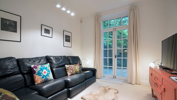 A living room with a black leather sofa, a fur rug, a television, and framed pictures on the wall. - Apartment 2 The Grove (Durham)