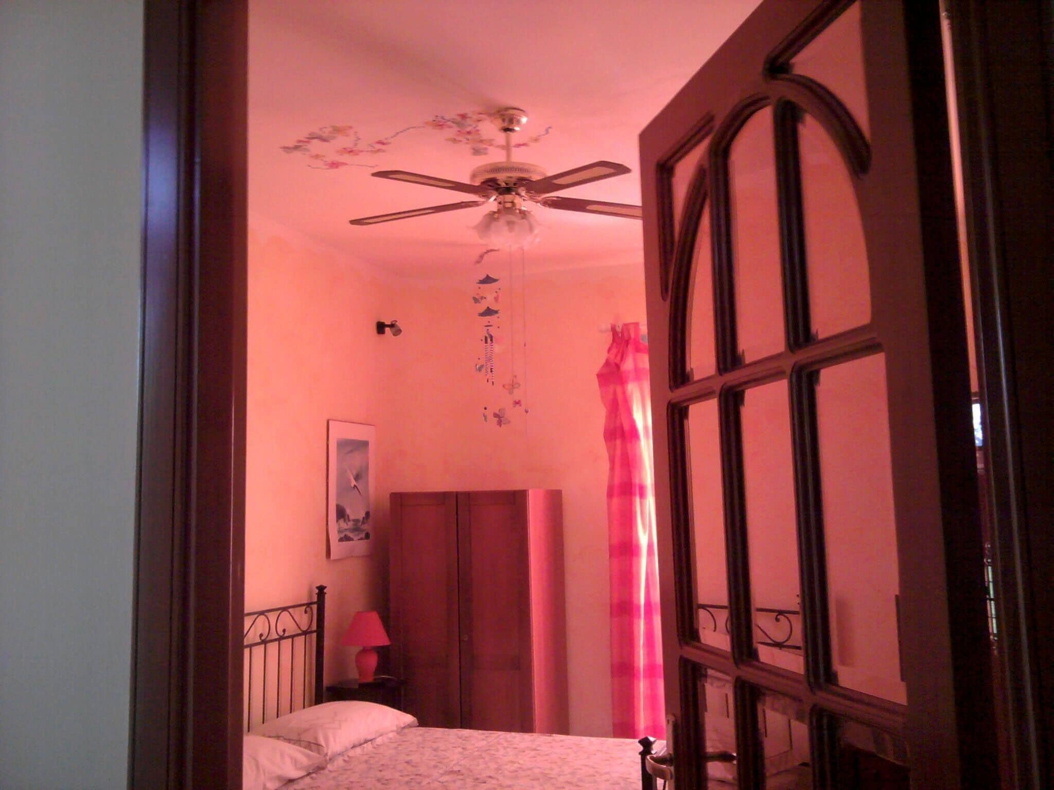 A bedroom with a bed, a ceiling fan, a window with curtains, and a door.
