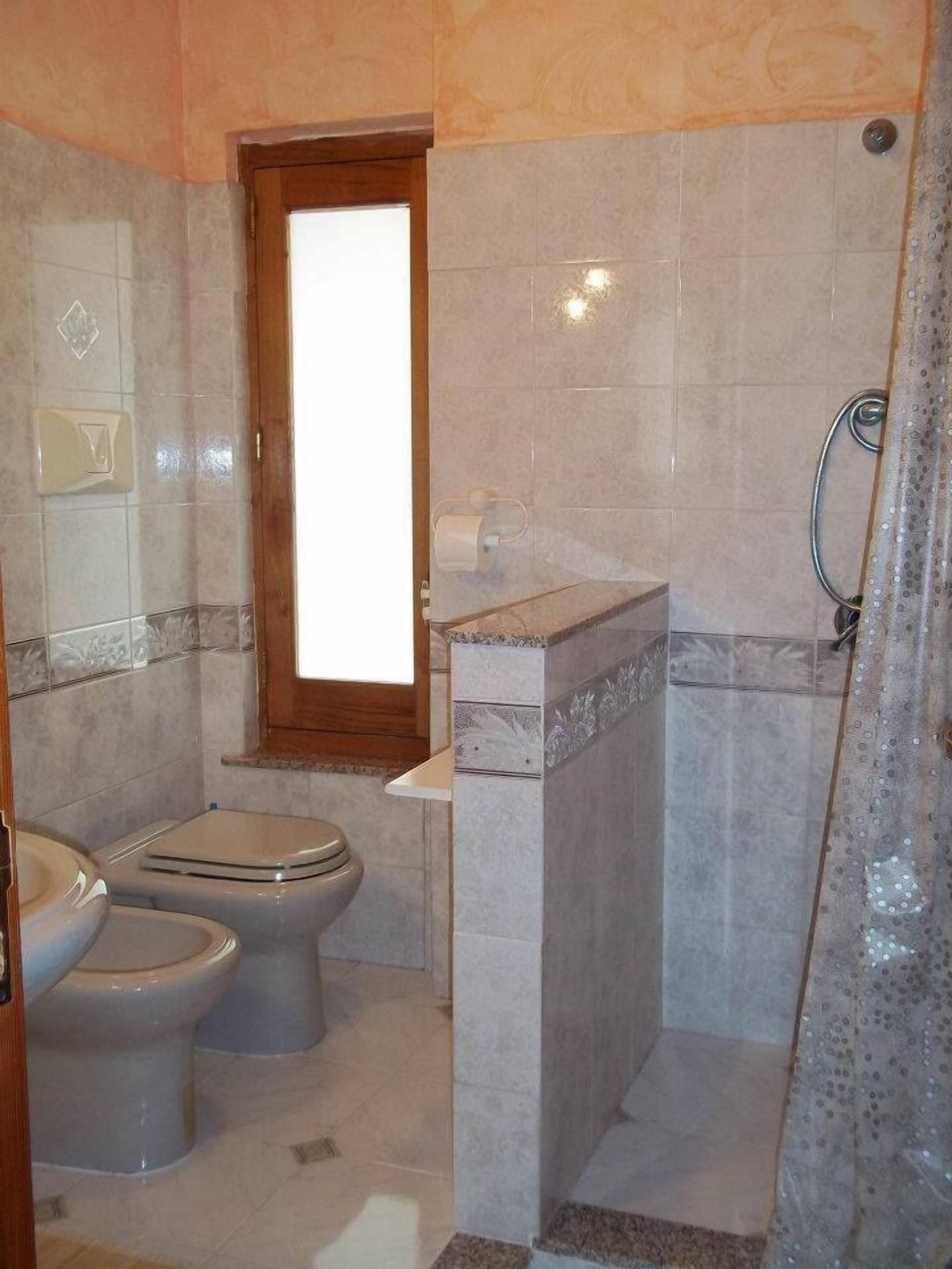 A bathroom with two toilets, a shower, and a window.