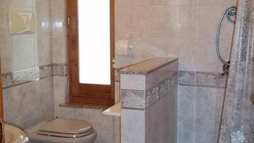 A bathroom with two toilets, a shower, and a window.