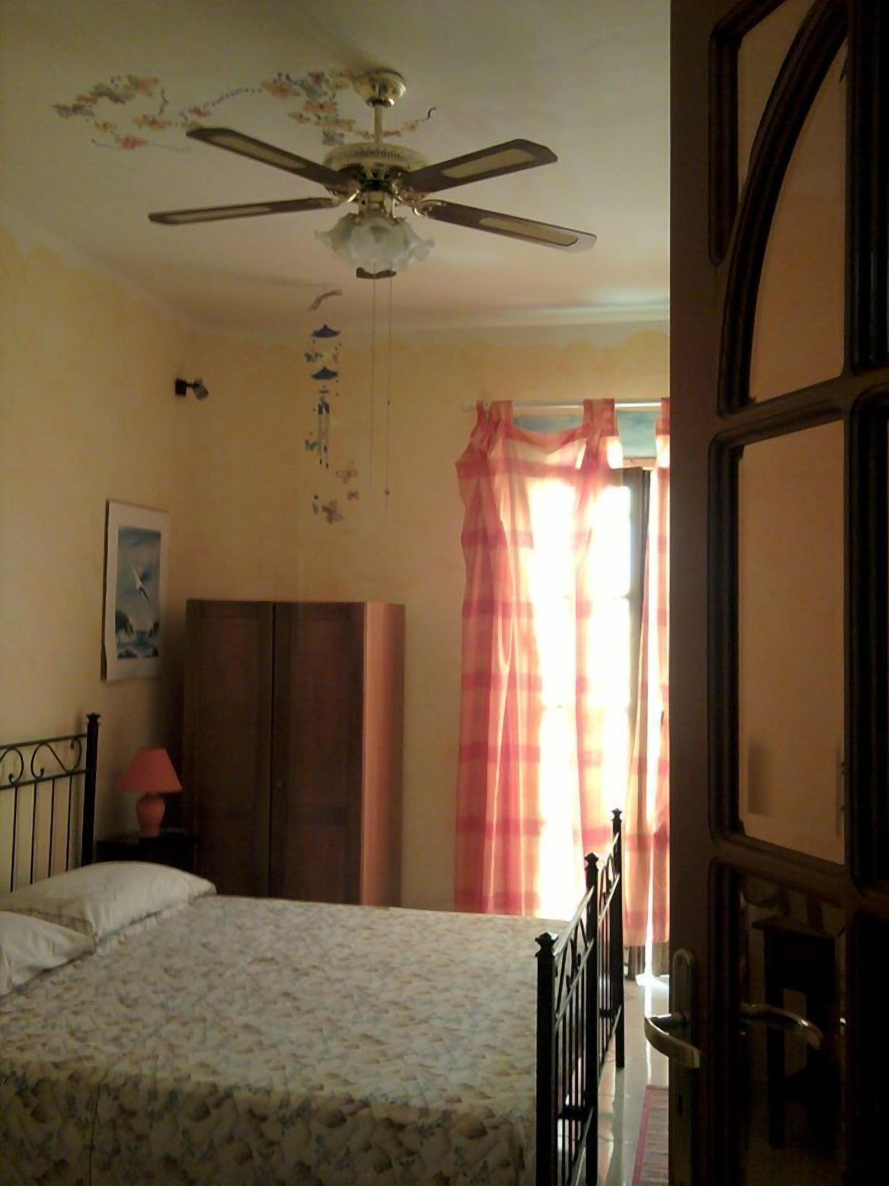 Ein Schlafzimmer mit Bett, Kleiderschrank, Deckenventilator und einem Fenster mit Vorhängen.
