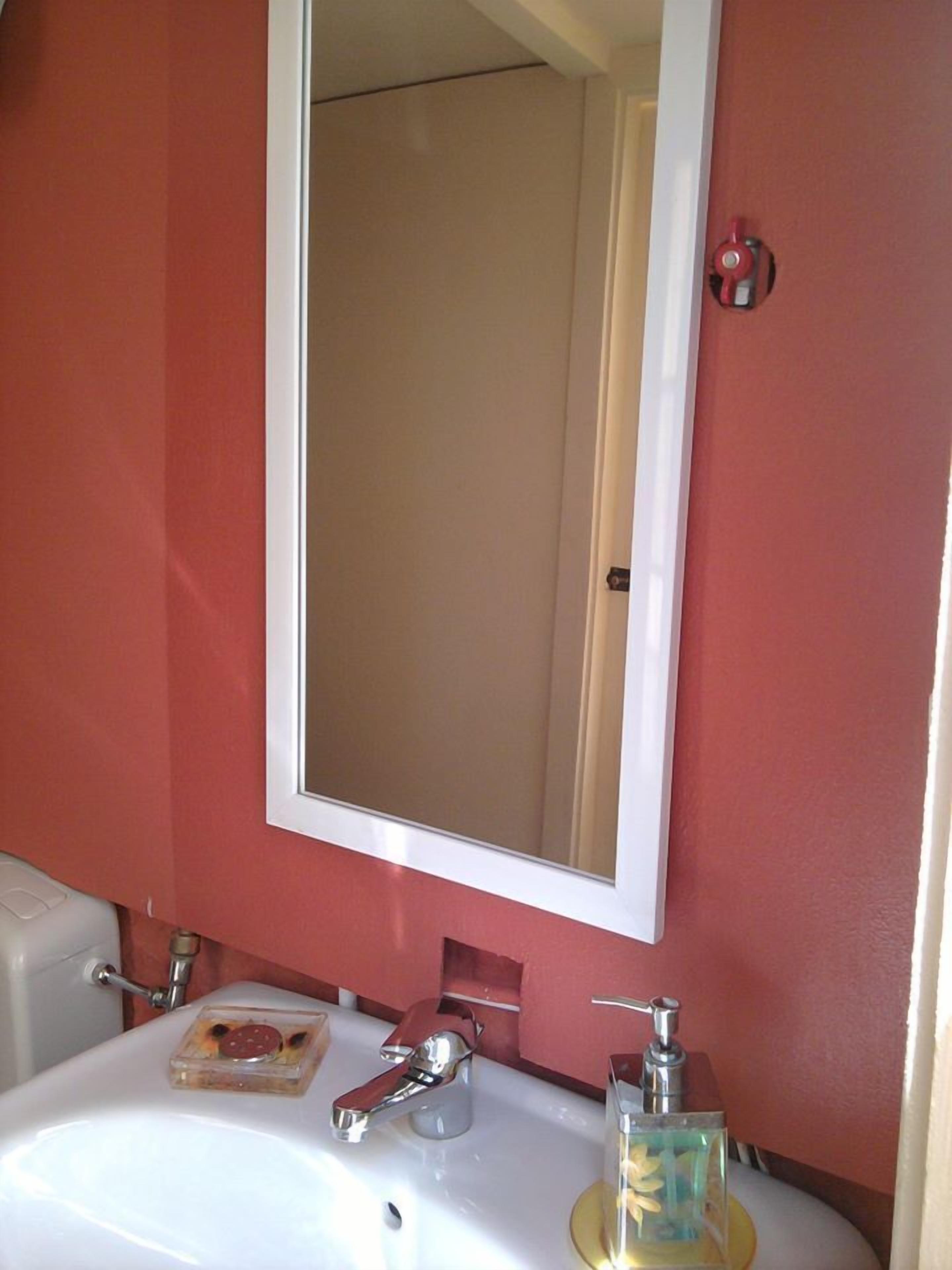 Une salle de bain avec un lavabo blanc, un miroir et un mur rouge.