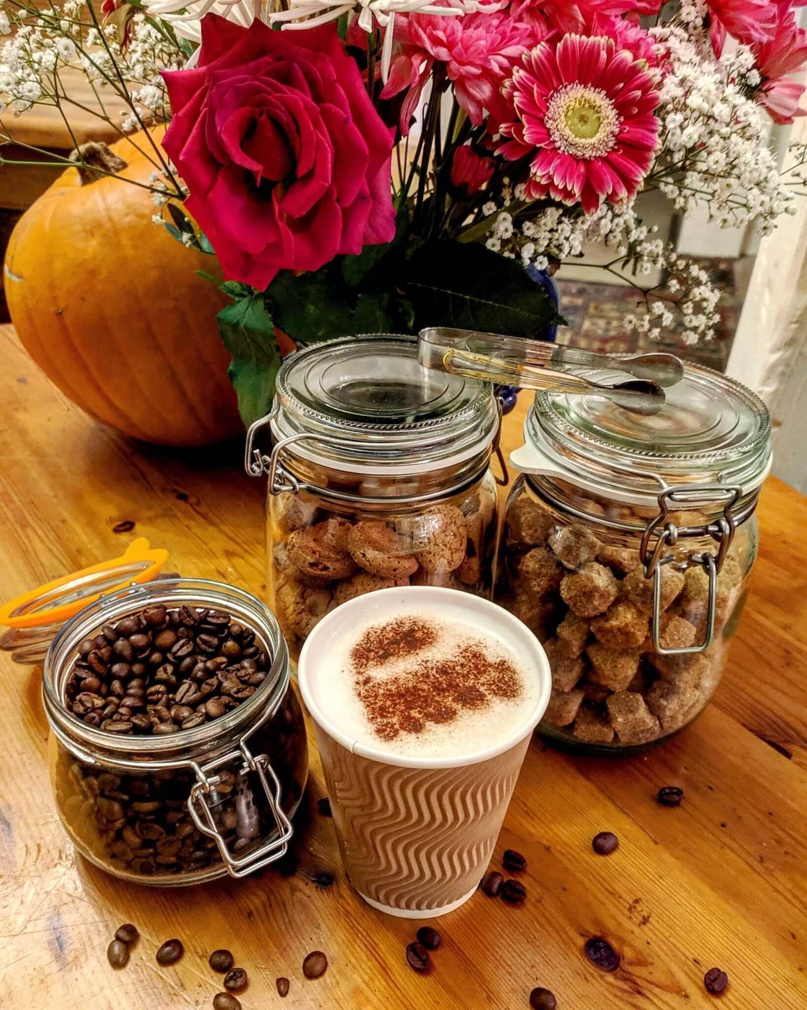 A table with three glass jars containing coffee beans and spices, a pumpkin, and a vase with flowers.