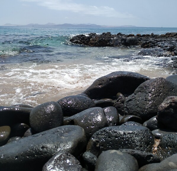 A rocky shoreline with waves crashing onto the beach. - Cozy apartment in quiet complex seafront 5 minutes from the beach (Costa Teguise)