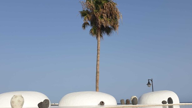 A beach with white domed structures, a palm tree, and a lamp post.