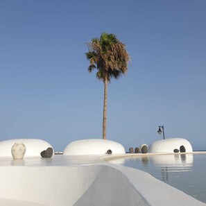 A beach with white domed structures, a palm tree, and a lamp post. - Cozy apartment in quiet complex seafront 5 minutes from the beach (Costa Teguise)