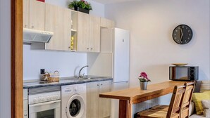 A compact kitchen with wooden cabinets, a built-in oven, a washing machine, and a dining area with a wooden table and chairs.