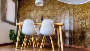 A dining area with a wooden table and white chairs, a potted plant, and a stone wall.