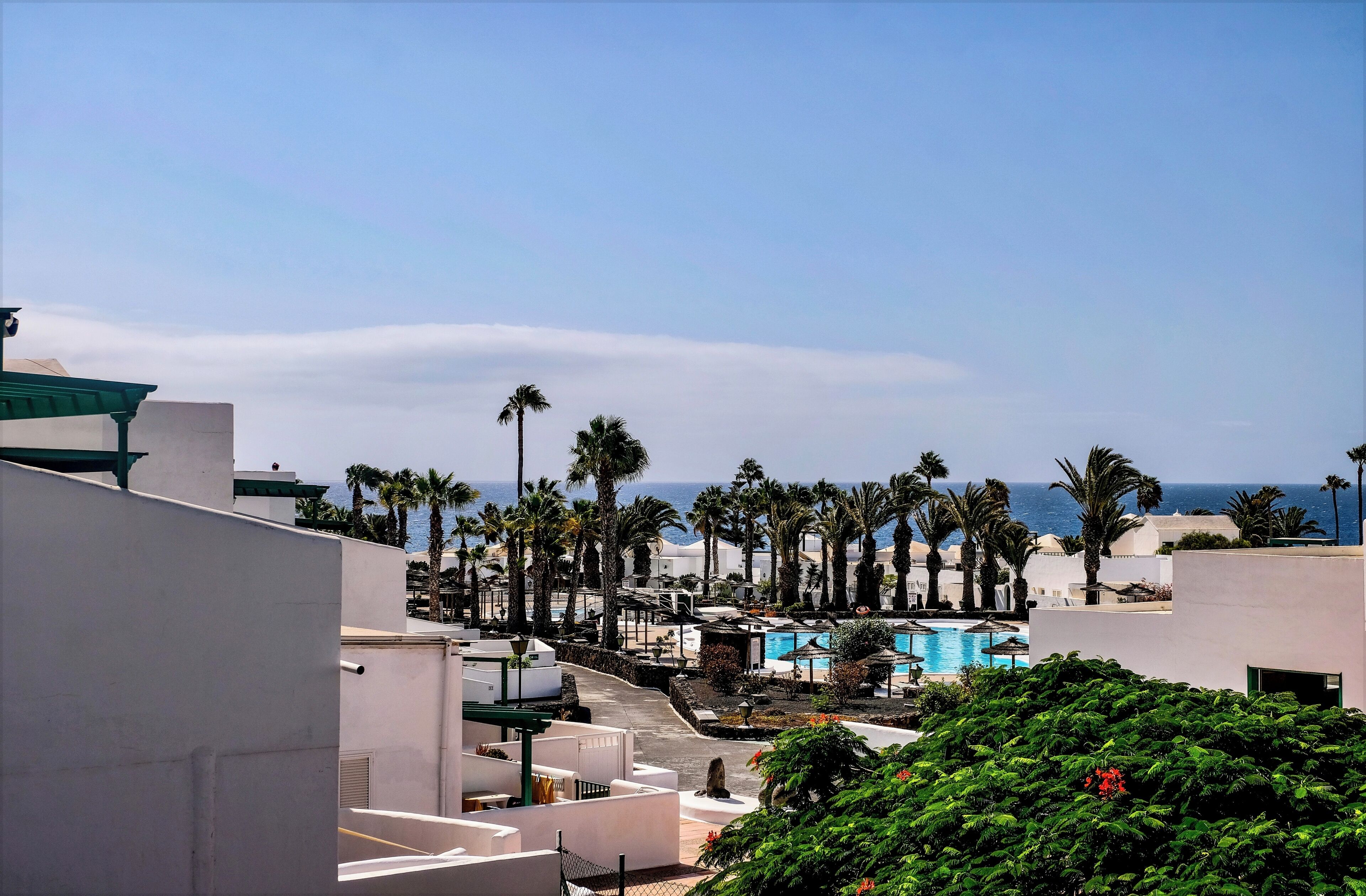 A resort with a pool, palm trees, and a view of the sea.