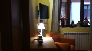 A room with a bed, a desk with a lamp, a chair, a television mounted on the wall, and a window with curtains.