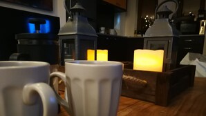 Two white ceramic mugs on a wooden table with a lit candle in the background.