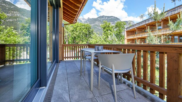 Un balcón con mesa y sillas, con vistas a un paisaje montañoso y un edificio de madera.