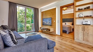 Una sala moderna con un sofá gris, un televisor montado en una pared de madera y un mueble de madera con electrodomésticos de cocina.