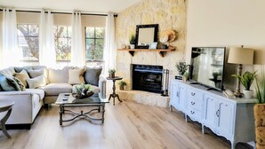 A living room with a stone fireplace, a sofa, a coffee table, and a TV on a cabinet. - 🌟LOCATION! Very Nice 2 BD 2BA Directly Across From Resort-Pool Grill Sleeps 6🏊 (Horseshoe Bay)