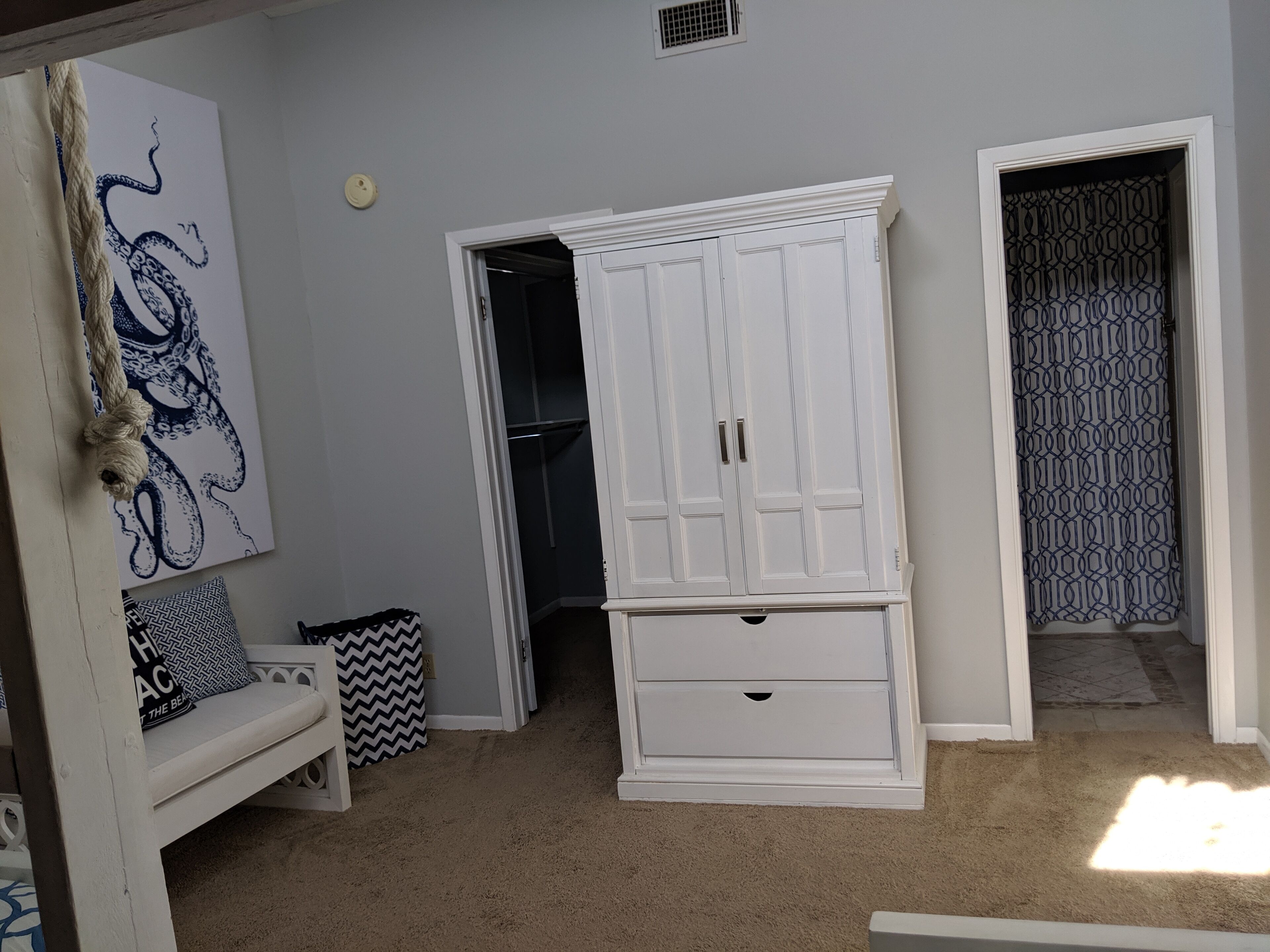 A room with a white wardrobe, a bench with patterned cushions, and a wall with a blue abstract design.