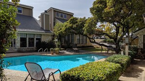 A swimming pool with a chair and potted plants, surrounded by stone buildings and trees. - 🌟LOCATION! Very Nice 2 BD 2BA Directly Across From Resort-Pool Grill Sleeps 6🏊 (Horseshoe Bay)