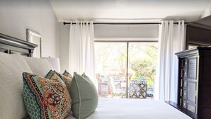 A bedroom with a large bed, white bedding, patterned pillows, a dark wooden dresser, and a view of the outdoors through a sliding glass door. - 🌟LOCATION! Very Nice 2 BD 2BA Directly Across From Resort-Pool Grill Sleeps 6🏊 (Horseshoe Bay)