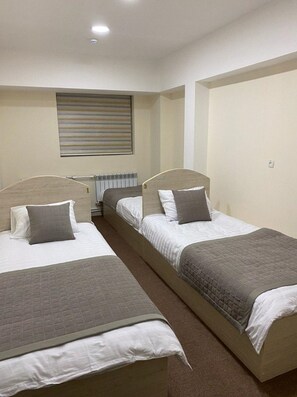 A room with two single beds, a radiator, and a window with blinds.