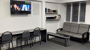 A modern waiting area with a sofa, chairs, a TV, and a bookshelf. - Hostel Paradise inn (Tashkent)