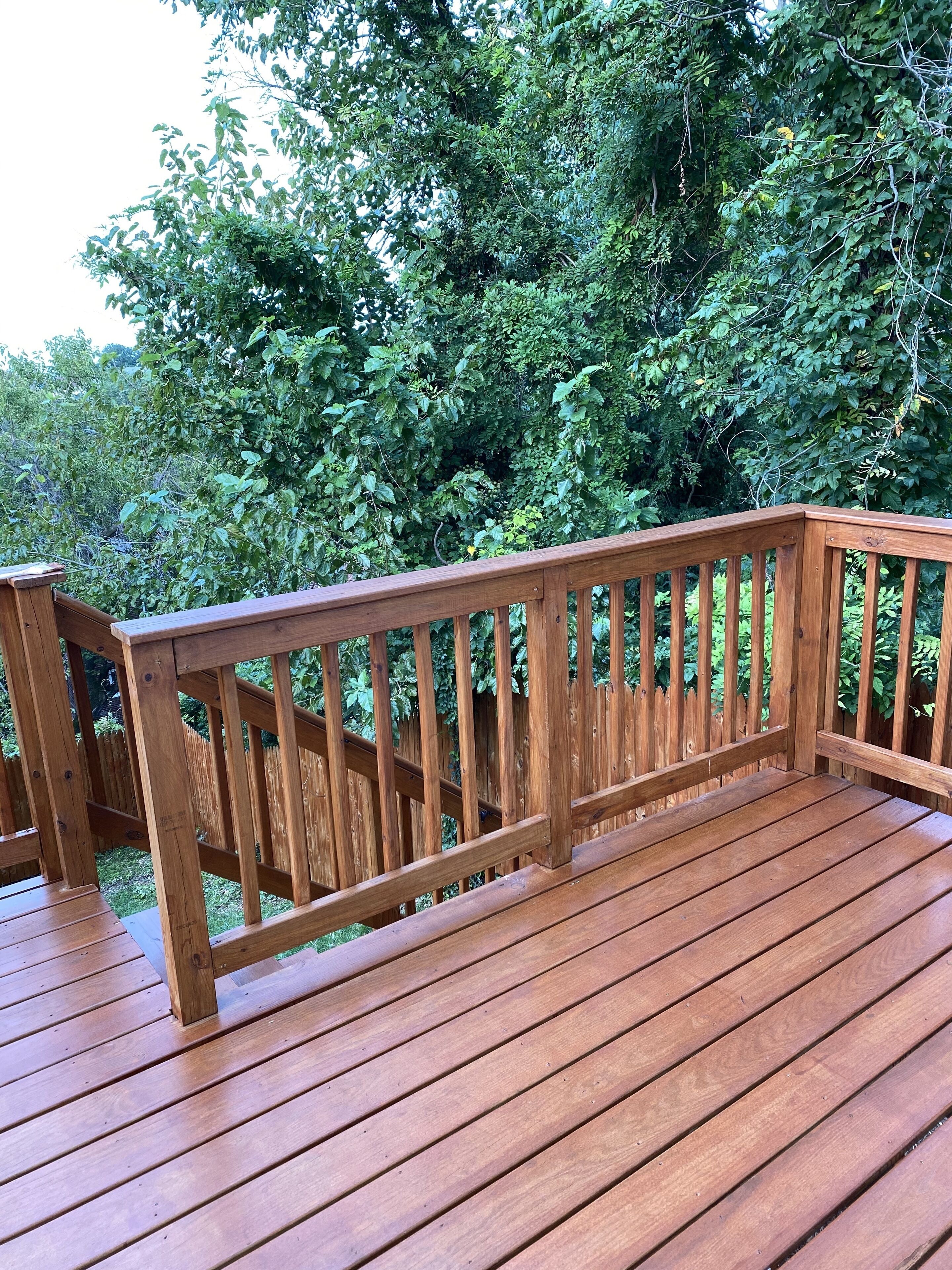Eine Holzterrasse mit Geländern, umgeben von dichtem Grün.