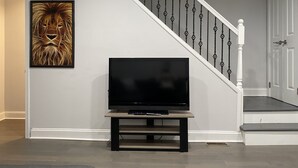 Eine Treppe mit schwarzer Geländer und weißen Spindeln, ein Flachbildfernseher auf einem Holzständer und ein gerahmtes Bild an der Wand.