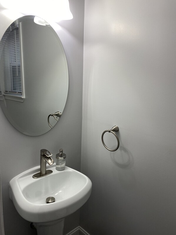 A bathroom with a white sink, a round mirror, and a towel ring on the wall. - Renovated Large Home (Washington)
