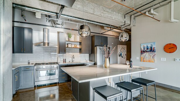 A modern kitchen with stainless steel appliances, a large island with bar stools, and exposed ductwork on the ceiling. - MINNeSTAY* Sable 901 - Penthouse | North Loop | Target Center (Minneapolis)