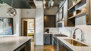 A modern kitchen with stainless steel appliances, a large island, and a view into the living area. - MINNeSTAY* Sable 901 - Penthouse | North Loop | Target Center (Minneapolis)