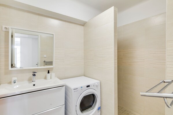 A modern bathroom with a white sink, mirror, and a front-loading washing machine.
