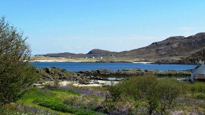 A coastal landscape with a rocky shoreline, a small body of water, and a few buildings in the distance. - Steading Holidays - Croft Caravan (Acharacle)
