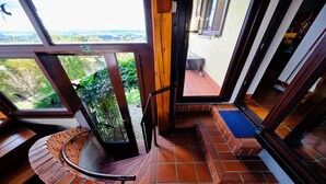 Eine Wendeltreppe führt zu einem Balkon mit Blick auf Grünflächen und eine entfernte Landschaft.
