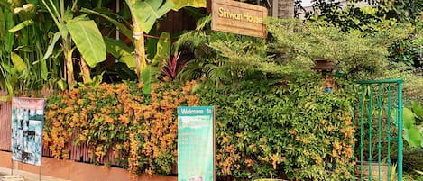 A signboard for Sriwan House with a list of amenities including an exotic garden, cozy environment, and clean rooms.
