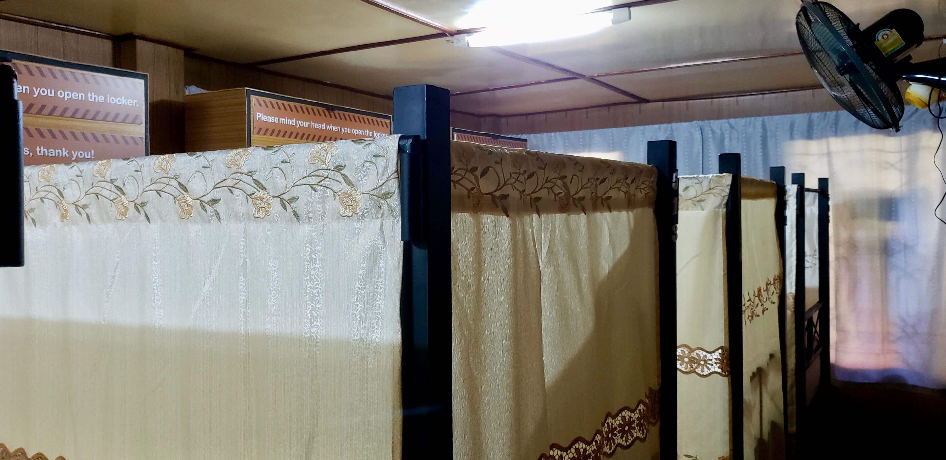A row of hotel rooms with curtains featuring floral patterns and a sign advising to mind your head when opening the locker.