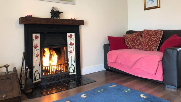 Una sala de estar con chimenea, un sofá con cojines rojo y dorado, una alfombra azul y un cuadro en la pared.