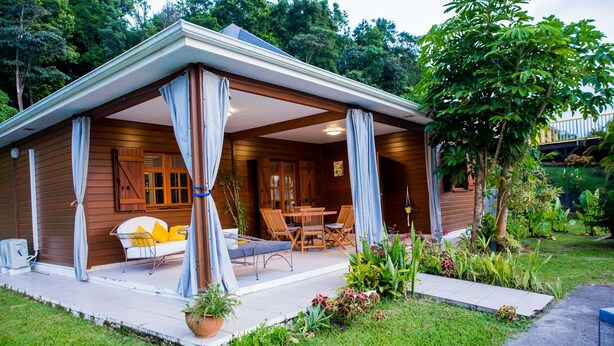 Una cabaña de madera con un porche cubierto, un comedor y un pequeño jardín.