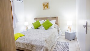 Un dormitorio con una cama, dos mesitas de noche, una lámpara de pie, aire acondicionado instalado en la pared, una alfombra estampada y una obra de arte con forma de mariposa.