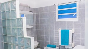 Un baño con cabina de ducha de vidrio, inodoro, lavadora y perchero.