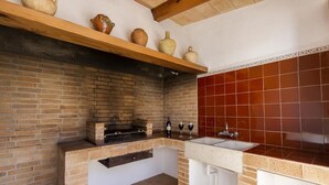 Una cocina con pared de ladrillo, repisa de madera con cerámica, estufa de ladrillo y salpicadero con azulejos rojos.