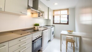 A modern kitchen with a built-in oven, microwave, and washing machine, a small dining table with two stools, and a window providing natural light. - "The QUEEN" New, fancy and relaxing. Beach & WIFI (València)