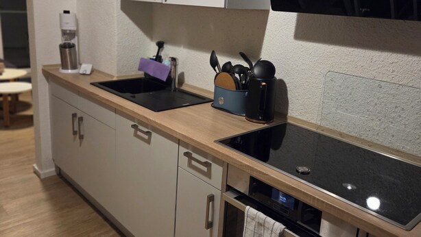 Une cuisine moderne dotée d’une plaque de cuisson à induction noire, d’un four en acier inoxydable et d’une machine à café posée sur le plan de travail.