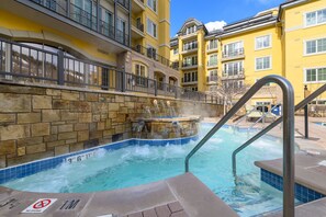 Piscina com muro de pedra e placa indicando 'proibido mergulhar', cercada por edifícios amarelos com varandas.