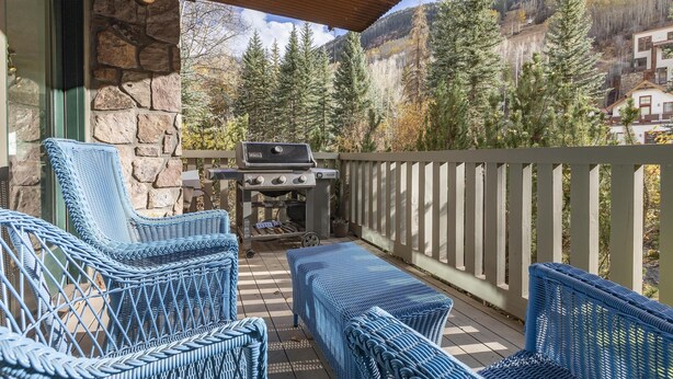 A covered patio with wicker furniture, a barbecue grill, and a scenic mountain view.