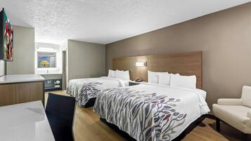 Habitación de hotel con dos camas, un escritorio, una silla y vistas a un edificio a través de una ventana.