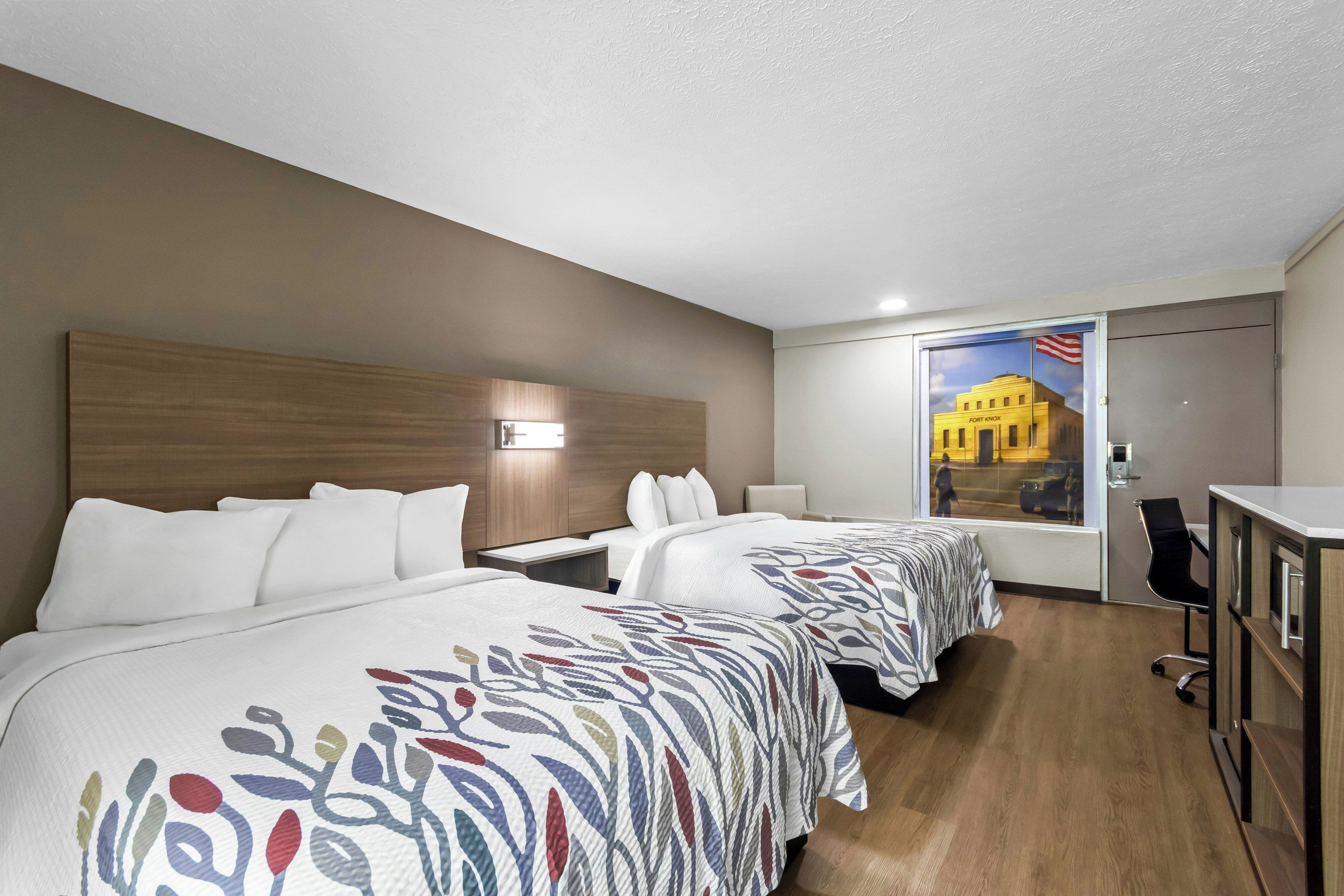 Une chambre d’hôtel avec deux lits, un bureau, une chaise et une grande fenêtre donnant sur un immeuble.
