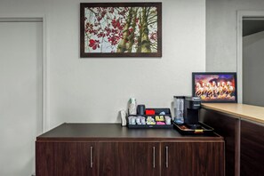 Ein Hotel-Empfangsbereich mit Kaffee-Ecke, gerahmten Kunstwerken und einem Fernseher.