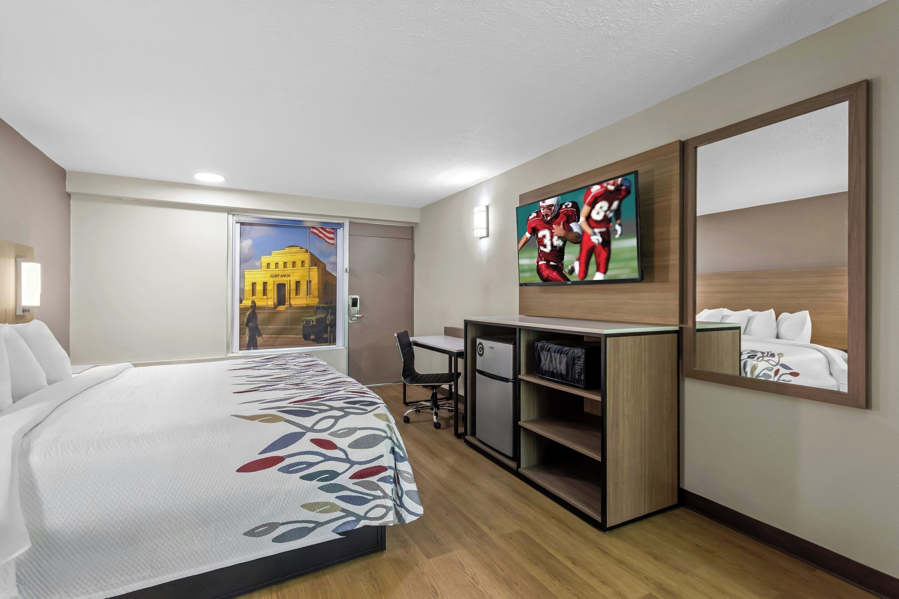 Ein Hotelzimmer mit Bett, Schreibtisch, Fernseher und einer Tür zu einem Flur.