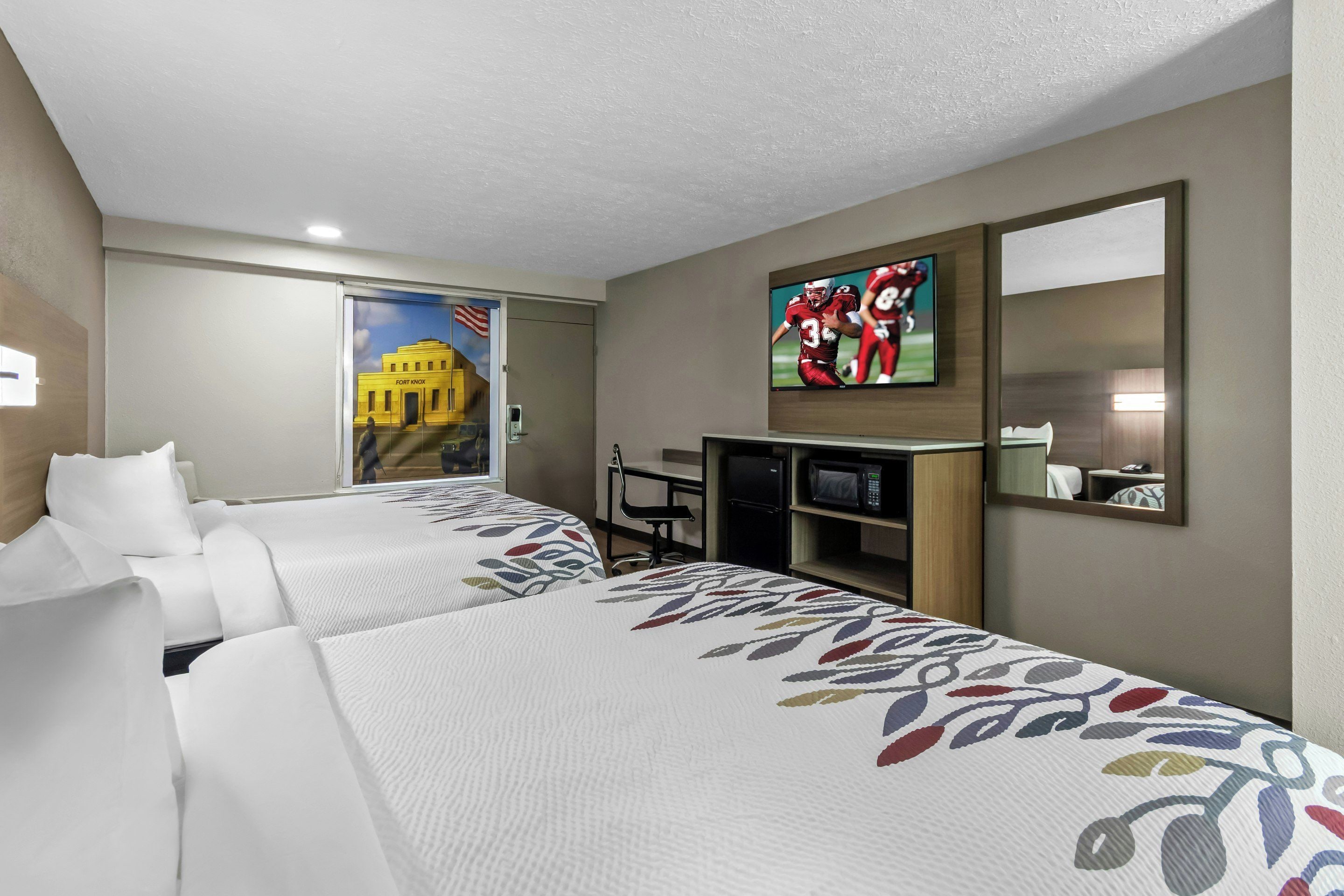 Een hotelkamer met twee bedden, een televisie, een bureau en een spiegel.