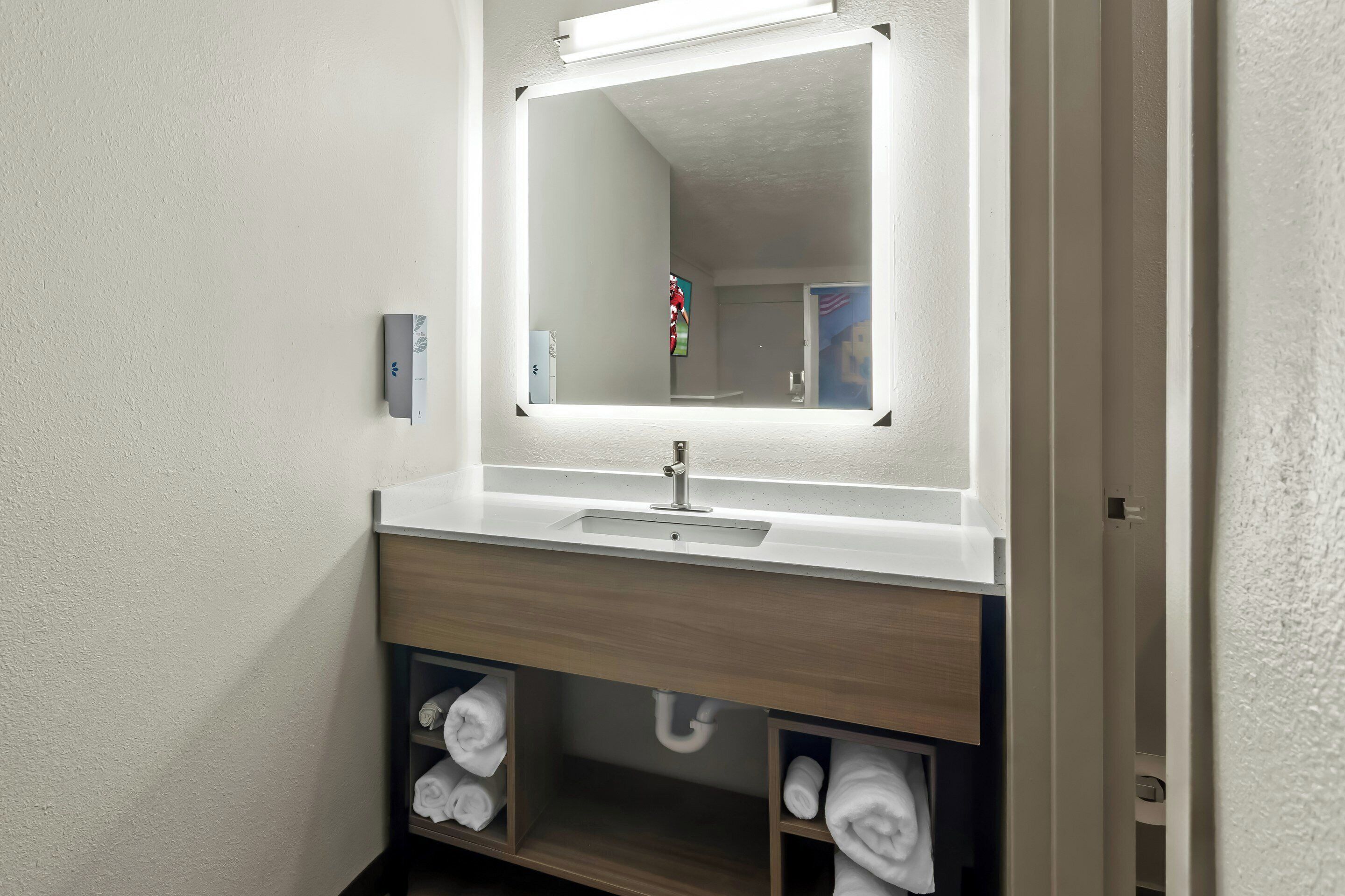 A bathroom with a white sink, mirror, and towel storage.