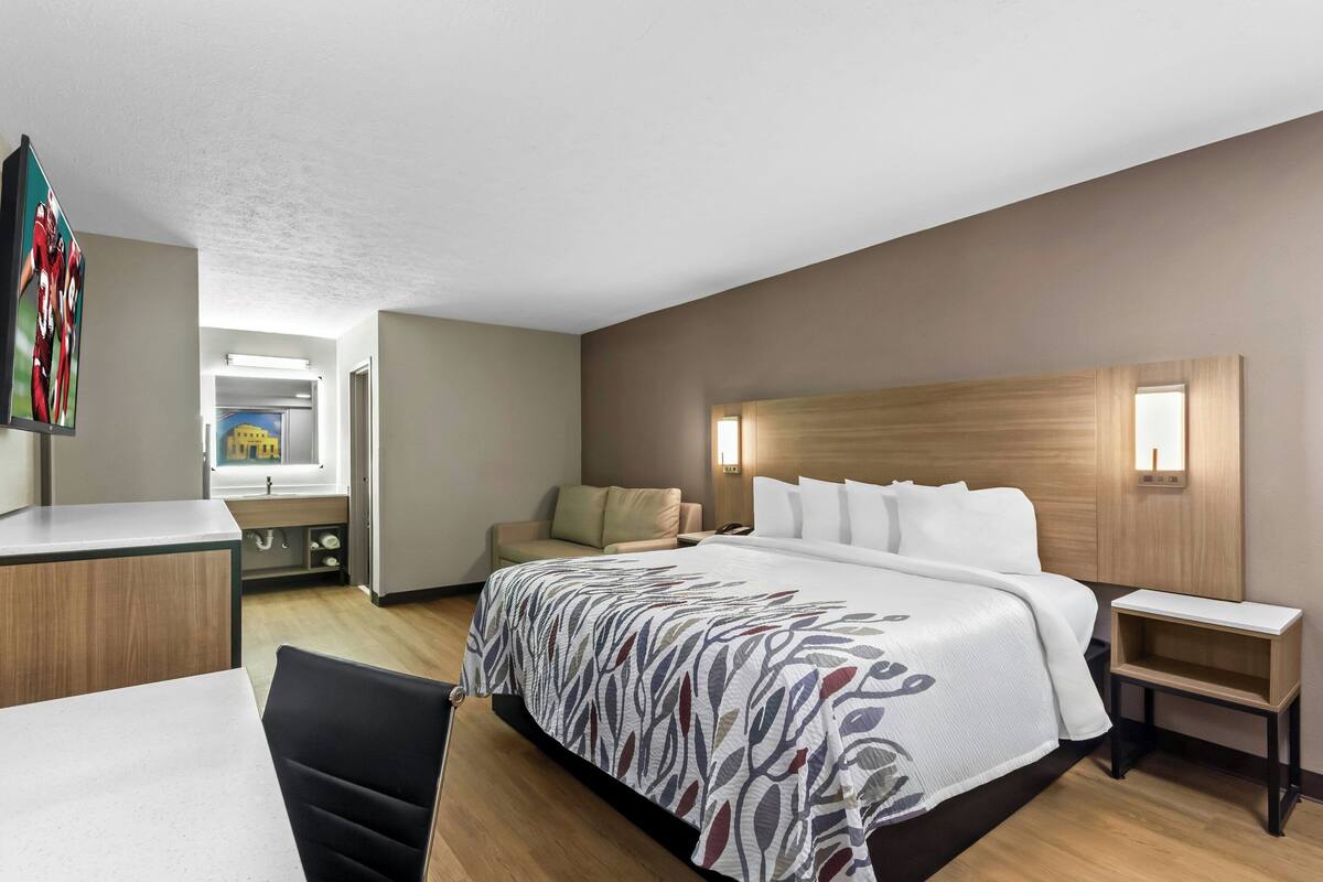 A hotel room with a bed, a desk, a chair, a sofa, and a small table.