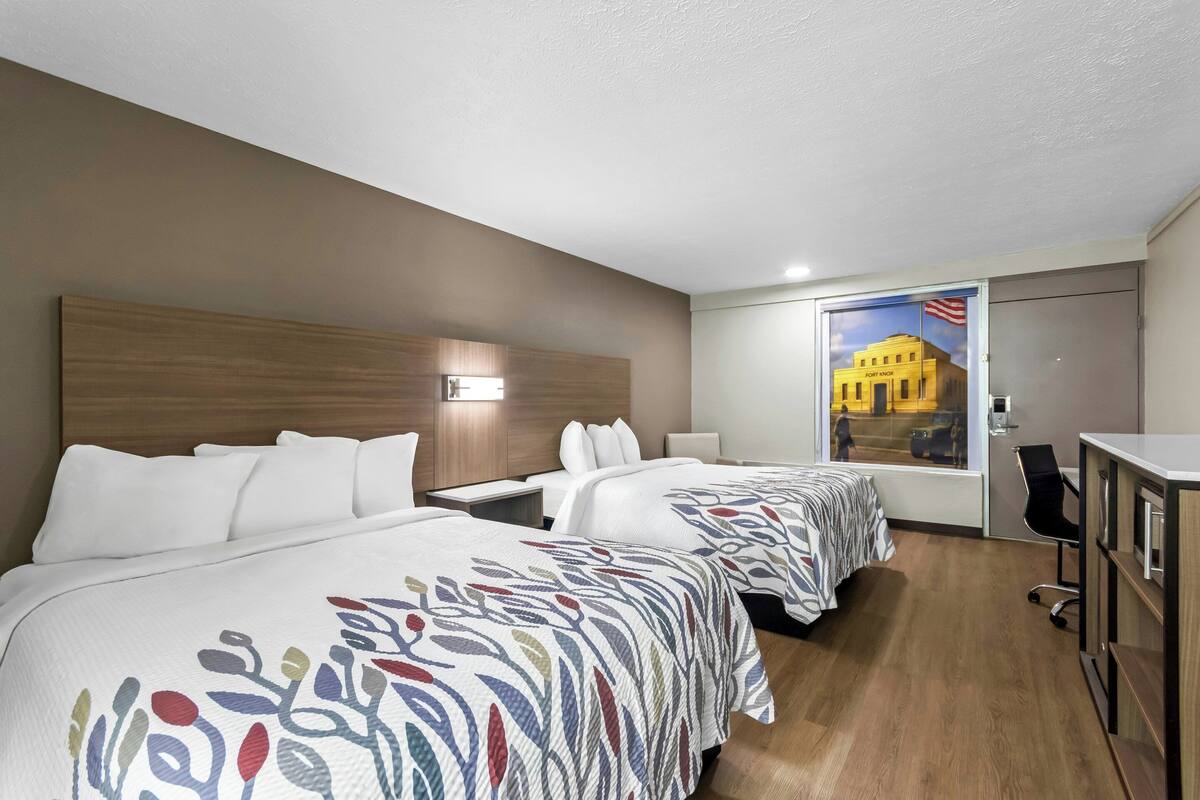 A hotel room with two beds, a desk, a chair, and a large window with a view of a building.